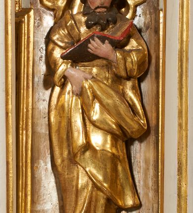 Zdjęcie nr 13: Tabernakulum architektoniczne, jednokondygnacyjne, pięcioosiowe. Osie wydzielone są sześcioma kanelowanymi kolumienkami na wysokich, profilowanych cokołach, z liściastymi kapitelami, podtrzymującymi profilowane belkowanie wyłamane na ich osiach. W polach pomiędzy kolumnami znajdują się nisze ujęte profilowaną ramą z uszakami. W czterech bocznych niszach, na trójdzielnych, profilowanych wspornikach stoją płaskorzeźbione postacie czterech ewangelistów na tle muszli palmetowych. Figurki są całopostaciowe, w ujęciu frontalnym, w złotych szatach, podtrzymują otwarte księgi, wskazując na tekst. Drzwiczki znajdują się na osi środkowej, zamknięte są półkoliście, płaskorzeźbione z przedstawieniem kielicha z koroną cierniową i z hostią w glorii promienistej. Kielich flankowany jest kłosami zbóż i winną latoroślą oraz winogronami. W partii belkowania płaskorzeźbiona dekoracja złożona z naprzemiennie ułożonych główek anielskich o złotych skrzydłach i płaskich rozetek. Tron wystawienia w formie baldachimu, z lambrekinem i chwostami, zwieńczony jest kulą z krzyżem, z podwieszonym z tyłu paludamentem podtrzymywanym przez parę puttów. Struktura polichromowana na biało, profile i detale pozłocone. 