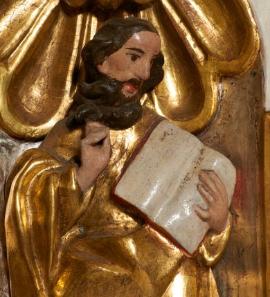 Zdjęcie nr 17: Tabernakulum architektoniczne, jednokondygnacyjne, pięcioosiowe. Osie wydzielone są sześcioma kanelowanymi kolumienkami na wysokich, profilowanych cokołach, z liściastymi kapitelami, podtrzymującymi profilowane belkowanie wyłamane na ich osiach. W polach pomiędzy kolumnami znajdują się nisze ujęte profilowaną ramą z uszakami. W czterech bocznych niszach, na trójdzielnych, profilowanych wspornikach stoją płaskorzeźbione postacie czterech ewangelistów na tle muszli palmetowych. Figurki są całopostaciowe, w ujęciu frontalnym, w złotych szatach, podtrzymują otwarte księgi, wskazując na tekst. Drzwiczki znajdują się na osi środkowej, zamknięte są półkoliście, płaskorzeźbione z przedstawieniem kielicha z koroną cierniową i z hostią w glorii promienistej. Kielich flankowany jest kłosami zbóż i winną latoroślą oraz winogronami. W partii belkowania płaskorzeźbiona dekoracja złożona z naprzemiennie ułożonych główek anielskich o złotych skrzydłach i płaskich rozetek. Tron wystawienia w formie baldachimu, z lambrekinem i chwostami, zwieńczony jest kulą z krzyżem, z podwieszonym z tyłu paludamentem podtrzymywanym przez parę puttów. Struktura polichromowana na biało, profile i detale pozłocone. 