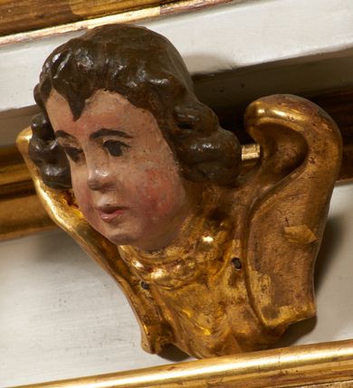 Zdjęcie nr 34: Tabernakulum architektoniczne, jednokondygnacyjne, pięcioosiowe. Osie wydzielone są sześcioma kanelowanymi kolumienkami na wysokich, profilowanych cokołach, z liściastymi kapitelami, podtrzymującymi profilowane belkowanie wyłamane na ich osiach. W polach pomiędzy kolumnami znajdują się nisze ujęte profilowaną ramą z uszakami. W czterech bocznych niszach, na trójdzielnych, profilowanych wspornikach stoją płaskorzeźbione postacie czterech ewangelistów na tle muszli palmetowych. Figurki są całopostaciowe, w ujęciu frontalnym, w złotych szatach, podtrzymują otwarte księgi, wskazując na tekst. Drzwiczki znajdują się na osi środkowej, zamknięte są półkoliście, płaskorzeźbione z przedstawieniem kielicha z koroną cierniową i z hostią w glorii promienistej. Kielich flankowany jest kłosami zbóż i winną latoroślą oraz winogronami. W partii belkowania płaskorzeźbiona dekoracja złożona z naprzemiennie ułożonych główek anielskich o złotych skrzydłach i płaskich rozetek. Tron wystawienia w formie baldachimu, z lambrekinem i chwostami, zwieńczony jest kulą z krzyżem, z podwieszonym z tyłu paludamentem podtrzymywanym przez parę puttów. Struktura polichromowana na biało, profile i detale pozłocone. 