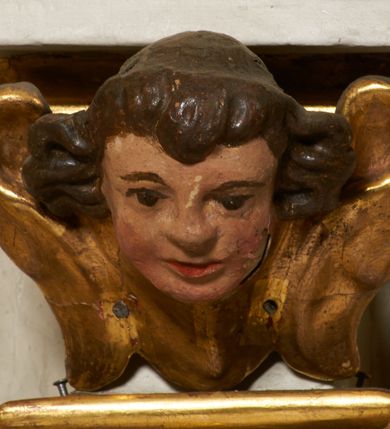 Zdjęcie nr 37: Tabernakulum architektoniczne, jednokondygnacyjne, pięcioosiowe. Osie wydzielone są sześcioma kanelowanymi kolumienkami na wysokich, profilowanych cokołach, z liściastymi kapitelami, podtrzymującymi profilowane belkowanie wyłamane na ich osiach. W polach pomiędzy kolumnami znajdują się nisze ujęte profilowaną ramą z uszakami. W czterech bocznych niszach, na trójdzielnych, profilowanych wspornikach stoją płaskorzeźbione postacie czterech ewangelistów na tle muszli palmetowych. Figurki są całopostaciowe, w ujęciu frontalnym, w złotych szatach, podtrzymują otwarte księgi, wskazując na tekst. Drzwiczki znajdują się na osi środkowej, zamknięte są półkoliście, płaskorzeźbione z przedstawieniem kielicha z koroną cierniową i z hostią w glorii promienistej. Kielich flankowany jest kłosami zbóż i winną latoroślą oraz winogronami. W partii belkowania płaskorzeźbiona dekoracja złożona z naprzemiennie ułożonych główek anielskich o złotych skrzydłach i płaskich rozetek. Tron wystawienia w formie baldachimu, z lambrekinem i chwostami, zwieńczony jest kulą z krzyżem, z podwieszonym z tyłu paludamentem podtrzymywanym przez parę puttów. Struktura polichromowana na biało, profile i detale pozłocone. 