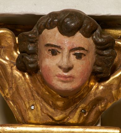 Zdjęcie nr 32: Tabernakulum architektoniczne, jednokondygnacyjne, pięcioosiowe. Osie wydzielone są sześcioma kanelowanymi kolumienkami na wysokich, profilowanych cokołach, z liściastymi kapitelami, podtrzymującymi profilowane belkowanie wyłamane na ich osiach. W polach pomiędzy kolumnami znajdują się nisze ujęte profilowaną ramą z uszakami. W czterech bocznych niszach, na trójdzielnych, profilowanych wspornikach stoją płaskorzeźbione postacie czterech ewangelistów na tle muszli palmetowych. Figurki są całopostaciowe, w ujęciu frontalnym, w złotych szatach, podtrzymują otwarte księgi, wskazując na tekst. Drzwiczki znajdują się na osi środkowej, zamknięte są półkoliście, płaskorzeźbione z przedstawieniem kielicha z koroną cierniową i z hostią w glorii promienistej. Kielich flankowany jest kłosami zbóż i winną latoroślą oraz winogronami. W partii belkowania płaskorzeźbiona dekoracja złożona z naprzemiennie ułożonych główek anielskich o złotych skrzydłach i płaskich rozetek. Tron wystawienia w formie baldachimu, z lambrekinem i chwostami, zwieńczony jest kulą z krzyżem, z podwieszonym z tyłu paludamentem podtrzymywanym przez parę puttów. Struktura polichromowana na biało, profile i detale pozłocone. 