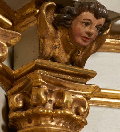 Zdjęcie nr 36: Tabernakulum architektoniczne, jednokondygnacyjne, pięcioosiowe. Osie wydzielone są sześcioma kanelowanymi kolumienkami na wysokich, profilowanych cokołach, z liściastymi kapitelami, podtrzymującymi profilowane belkowanie wyłamane na ich osiach. W polach pomiędzy kolumnami znajdują się nisze ujęte profilowaną ramą z uszakami. W czterech bocznych niszach, na trójdzielnych, profilowanych wspornikach stoją płaskorzeźbione postacie czterech ewangelistów na tle muszli palmetowych. Figurki są całopostaciowe, w ujęciu frontalnym, w złotych szatach, podtrzymują otwarte księgi, wskazując na tekst. Drzwiczki znajdują się na osi środkowej, zamknięte są półkoliście, płaskorzeźbione z przedstawieniem kielicha z koroną cierniową i z hostią w glorii promienistej. Kielich flankowany jest kłosami zbóż i winną latoroślą oraz winogronami. W partii belkowania płaskorzeźbiona dekoracja złożona z naprzemiennie ułożonych główek anielskich o złotych skrzydłach i płaskich rozetek. Tron wystawienia w formie baldachimu, z lambrekinem i chwostami, zwieńczony jest kulą z krzyżem, z podwieszonym z tyłu paludamentem podtrzymywanym przez parę puttów. Struktura polichromowana na biało, profile i detale pozłocone. 