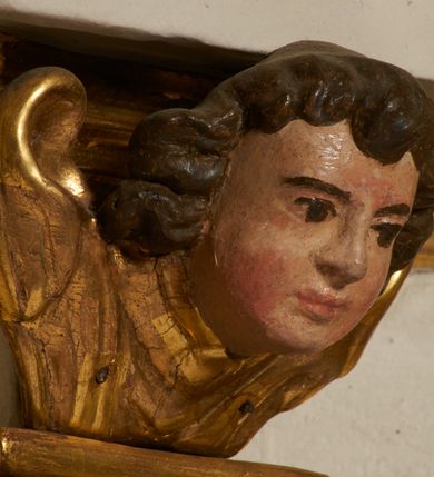 Zdjęcie nr 31: Tabernakulum architektoniczne, jednokondygnacyjne, pięcioosiowe. Osie wydzielone są sześcioma kanelowanymi kolumienkami na wysokich, profilowanych cokołach, z liściastymi kapitelami, podtrzymującymi profilowane belkowanie wyłamane na ich osiach. W polach pomiędzy kolumnami znajdują się nisze ujęte profilowaną ramą z uszakami. W czterech bocznych niszach, na trójdzielnych, profilowanych wspornikach stoją płaskorzeźbione postacie czterech ewangelistów na tle muszli palmetowych. Figurki są całopostaciowe, w ujęciu frontalnym, w złotych szatach, podtrzymują otwarte księgi, wskazując na tekst. Drzwiczki znajdują się na osi środkowej, zamknięte są półkoliście, płaskorzeźbione z przedstawieniem kielicha z koroną cierniową i z hostią w glorii promienistej. Kielich flankowany jest kłosami zbóż i winną latoroślą oraz winogronami. W partii belkowania płaskorzeźbiona dekoracja złożona z naprzemiennie ułożonych główek anielskich o złotych skrzydłach i płaskich rozetek. Tron wystawienia w formie baldachimu, z lambrekinem i chwostami, zwieńczony jest kulą z krzyżem, z podwieszonym z tyłu paludamentem podtrzymywanym przez parę puttów. Struktura polichromowana na biało, profile i detale pozłocone. 