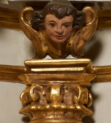 Zdjęcie nr 35: Tabernakulum architektoniczne, jednokondygnacyjne, pięcioosiowe. Osie wydzielone są sześcioma kanelowanymi kolumienkami na wysokich, profilowanych cokołach, z liściastymi kapitelami, podtrzymującymi profilowane belkowanie wyłamane na ich osiach. W polach pomiędzy kolumnami znajdują się nisze ujęte profilowaną ramą z uszakami. W czterech bocznych niszach, na trójdzielnych, profilowanych wspornikach stoją płaskorzeźbione postacie czterech ewangelistów na tle muszli palmetowych. Figurki są całopostaciowe, w ujęciu frontalnym, w złotych szatach, podtrzymują otwarte księgi, wskazując na tekst. Drzwiczki znajdują się na osi środkowej, zamknięte są półkoliście, płaskorzeźbione z przedstawieniem kielicha z koroną cierniową i z hostią w glorii promienistej. Kielich flankowany jest kłosami zbóż i winną latoroślą oraz winogronami. W partii belkowania płaskorzeźbiona dekoracja złożona z naprzemiennie ułożonych główek anielskich o złotych skrzydłach i płaskich rozetek. Tron wystawienia w formie baldachimu, z lambrekinem i chwostami, zwieńczony jest kulą z krzyżem, z podwieszonym z tyłu paludamentem podtrzymywanym przez parę puttów. Struktura polichromowana na biało, profile i detale pozłocone. 