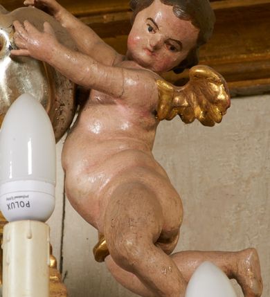 Zdjęcie nr 27: Tabernakulum architektoniczne, jednokondygnacyjne, pięcioosiowe. Osie wydzielone są sześcioma kanelowanymi kolumienkami na wysokich, profilowanych cokołach, z liściastymi kapitelami, podtrzymującymi profilowane belkowanie wyłamane na ich osiach. W polach pomiędzy kolumnami znajdują się nisze ujęte profilowaną ramą z uszakami. W czterech bocznych niszach, na trójdzielnych, profilowanych wspornikach stoją płaskorzeźbione postacie czterech ewangelistów na tle muszli palmetowych. Figurki są całopostaciowe, w ujęciu frontalnym, w złotych szatach, podtrzymują otwarte księgi, wskazując na tekst. Drzwiczki znajdują się na osi środkowej, zamknięte są półkoliście, płaskorzeźbione z przedstawieniem kielicha z koroną cierniową i z hostią w glorii promienistej. Kielich flankowany jest kłosami zbóż i winną latoroślą oraz winogronami. W partii belkowania płaskorzeźbiona dekoracja złożona z naprzemiennie ułożonych główek anielskich o złotych skrzydłach i płaskich rozetek. Tron wystawienia w formie baldachimu, z lambrekinem i chwostami, zwieńczony jest kulą z krzyżem, z podwieszonym z tyłu paludamentem podtrzymywanym przez parę puttów. Struktura polichromowana na biało, profile i detale pozłocone. 