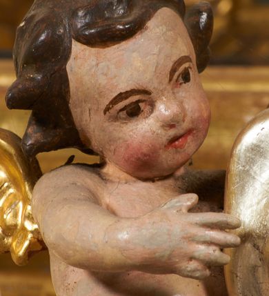 Zdjęcie nr 25: Tabernakulum architektoniczne, jednokondygnacyjne, pięcioosiowe. Osie wydzielone są sześcioma kanelowanymi kolumienkami na wysokich, profilowanych cokołach, z liściastymi kapitelami, podtrzymującymi profilowane belkowanie wyłamane na ich osiach. W polach pomiędzy kolumnami znajdują się nisze ujęte profilowaną ramą z uszakami. W czterech bocznych niszach, na trójdzielnych, profilowanych wspornikach stoją płaskorzeźbione postacie czterech ewangelistów na tle muszli palmetowych. Figurki są całopostaciowe, w ujęciu frontalnym, w złotych szatach, podtrzymują otwarte księgi, wskazując na tekst. Drzwiczki znajdują się na osi środkowej, zamknięte są półkoliście, płaskorzeźbione z przedstawieniem kielicha z koroną cierniową i z hostią w glorii promienistej. Kielich flankowany jest kłosami zbóż i winną latoroślą oraz winogronami. W partii belkowania płaskorzeźbiona dekoracja złożona z naprzemiennie ułożonych główek anielskich o złotych skrzydłach i płaskich rozetek. Tron wystawienia w formie baldachimu, z lambrekinem i chwostami, zwieńczony jest kulą z krzyżem, z podwieszonym z tyłu paludamentem podtrzymywanym przez parę puttów. Struktura polichromowana na biało, profile i detale pozłocone. 