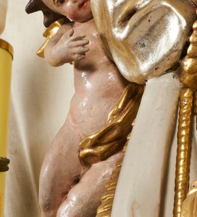 Zdjęcie nr 24: Tabernakulum architektoniczne, jednokondygnacyjne, pięcioosiowe. Osie wydzielone są sześcioma kanelowanymi kolumienkami na wysokich, profilowanych cokołach, z liściastymi kapitelami, podtrzymującymi profilowane belkowanie wyłamane na ich osiach. W polach pomiędzy kolumnami znajdują się nisze ujęte profilowaną ramą z uszakami. W czterech bocznych niszach, na trójdzielnych, profilowanych wspornikach stoją płaskorzeźbione postacie czterech ewangelistów na tle muszli palmetowych. Figurki są całopostaciowe, w ujęciu frontalnym, w złotych szatach, podtrzymują otwarte księgi, wskazując na tekst. Drzwiczki znajdują się na osi środkowej, zamknięte są półkoliście, płaskorzeźbione z przedstawieniem kielicha z koroną cierniową i z hostią w glorii promienistej. Kielich flankowany jest kłosami zbóż i winną latoroślą oraz winogronami. W partii belkowania płaskorzeźbiona dekoracja złożona z naprzemiennie ułożonych główek anielskich o złotych skrzydłach i płaskich rozetek. Tron wystawienia w formie baldachimu, z lambrekinem i chwostami, zwieńczony jest kulą z krzyżem, z podwieszonym z tyłu paludamentem podtrzymywanym przez parę puttów. Struktura polichromowana na biało, profile i detale pozłocone. 