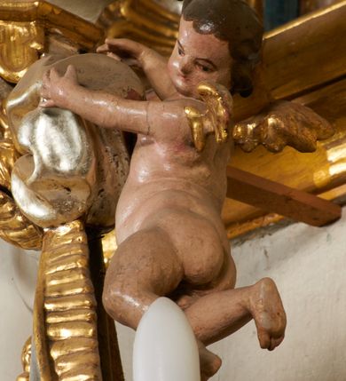 Zdjęcie nr 28: Tabernakulum architektoniczne, jednokondygnacyjne, pięcioosiowe. Osie wydzielone są sześcioma kanelowanymi kolumienkami na wysokich, profilowanych cokołach, z liściastymi kapitelami, podtrzymującymi profilowane belkowanie wyłamane na ich osiach. W polach pomiędzy kolumnami znajdują się nisze ujęte profilowaną ramą z uszakami. W czterech bocznych niszach, na trójdzielnych, profilowanych wspornikach stoją płaskorzeźbione postacie czterech ewangelistów na tle muszli palmetowych. Figurki są całopostaciowe, w ujęciu frontalnym, w złotych szatach, podtrzymują otwarte księgi, wskazując na tekst. Drzwiczki znajdują się na osi środkowej, zamknięte są półkoliście, płaskorzeźbione z przedstawieniem kielicha z koroną cierniową i z hostią w glorii promienistej. Kielich flankowany jest kłosami zbóż i winną latoroślą oraz winogronami. W partii belkowania płaskorzeźbiona dekoracja złożona z naprzemiennie ułożonych główek anielskich o złotych skrzydłach i płaskich rozetek. Tron wystawienia w formie baldachimu, z lambrekinem i chwostami, zwieńczony jest kulą z krzyżem, z podwieszonym z tyłu paludamentem podtrzymywanym przez parę puttów. Struktura polichromowana na biało, profile i detale pozłocone. 