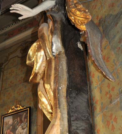 Zdjęcie nr 6: Obie rzeźby są ścięte z tyłu i głęboko drążone. Figury zwrócone są frontalnie z głowami skierowanymi w stronę ołtarza, stoją w kontrapoście. Anioł na lewej bramce unosi prawą rękę w górę, lewą opuszcza w dół. Anioł z prawej bramki prawą rękę kładzie na piersi, lewa zaś jest ugięta i i uniesiona. Anioły mają pociągłe twarze o uwypuklonych brodach, prostych, dużych nosach i szerokich nozdrzach, oczach o łukowatych górnych powiekach i półkolistych łukach brwiowych, pełnych ustach z wydrążonymi kącikami. Włosy opadające na plecy rzeźbione są w grube, falowane i zmierzwione pukle. Postacie ubrane są w tuniki przepasane w talii, przykrywające jedno ramię szerokim rękawem, odsłaniające część torsu i drugą rękę oraz w płaszcze zawinięte w partii ud. Polichromia w partiach ciała naturalistyczna, szaty pozłacane.  
