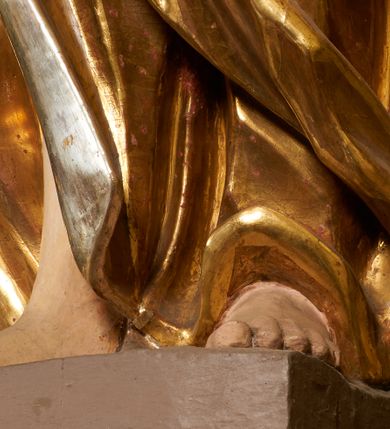 Zdjęcie nr 40: Obie rzeźby są ścięte z tyłu i głęboko drążone. Figury zwrócone są frontalnie z głowami skierowanymi w stronę ołtarza, stoją w kontrapoście. Anioł na lewej bramce unosi prawą rękę w górę, lewą opuszcza w dół. Anioł z prawej bramki prawą rękę kładzie na piersi, lewa zaś jest ugięta i i uniesiona. Anioły mają pociągłe twarze o uwypuklonych brodach, prostych, dużych nosach i szerokich nozdrzach, oczach o łukowatych górnych powiekach i półkolistych łukach brwiowych, pełnych ustach z wydrążonymi kącikami. Włosy opadające na plecy rzeźbione są w grube, falowane i zmierzwione pukle. Postacie ubrane są w tuniki przepasane w talii, przykrywające jedno ramię szerokim rękawem, odsłaniające część torsu i drugą rękę oraz w płaszcze zawinięte w partii ud. Polichromia w partiach ciała naturalistyczna, szaty pozłacane.  
