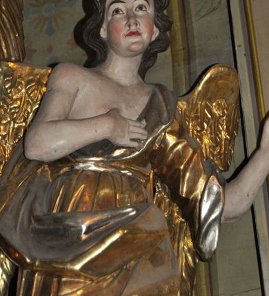 Zdjęcie nr 31: Obie rzeźby są ścięte z tyłu i głęboko drążone. Figury zwrócone są frontalnie z głowami skierowanymi w stronę ołtarza, stoją w kontrapoście. Anioł na lewej bramce unosi prawą rękę w górę, lewą opuszcza w dół. Anioł z prawej bramki prawą rękę kładzie na piersi, lewa zaś jest ugięta i i uniesiona. Anioły mają pociągłe twarze o uwypuklonych brodach, prostych, dużych nosach i szerokich nozdrzach, oczach o łukowatych górnych powiekach i półkolistych łukach brwiowych, pełnych ustach z wydrążonymi kącikami. Włosy opadające na plecy rzeźbione są w grube, falowane i zmierzwione pukle. Postacie ubrane są w tuniki przepasane w talii, przykrywające jedno ramię szerokim rękawem, odsłaniające część torsu i drugą rękę oraz w płaszcze zawinięte w partii ud. Polichromia w partiach ciała naturalistyczna, szaty pozłacane.  
