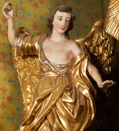 Zdjęcie nr 1: Obie rzeźby są ścięte z tyłu i głęboko drążone. Figury zwrócone są frontalnie z głowami skierowanymi w stronę ołtarza, stoją w kontrapoście. Anioł na lewej bramce unosi prawą rękę w górę, lewą opuszcza w dół. Anioł z prawej bramki prawą rękę kładzie na piersi, lewa zaś jest ugięta i i uniesiona. Anioły mają pociągłe twarze o uwypuklonych brodach, prostych, dużych nosach i szerokich nozdrzach, oczach o łukowatych górnych powiekach i półkolistych łukach brwiowych, pełnych ustach z wydrążonymi kącikami. Włosy opadające na plecy rzeźbione są w grube, falowane i zmierzwione pukle. Postacie ubrane są w tuniki przepasane w talii, przykrywające jedno ramię szerokim rękawem, odsłaniające część torsu i drugą rękę oraz w płaszcze zawinięte w partii ud. Polichromia w partiach ciała naturalistyczna, szaty pozłacane.  
