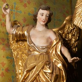 Zdjęcie nr 1: Obie rzeźby są ścięte z tyłu i głęboko drążone. Figury zwrócone są frontalnie z głowami skierowanymi w stronę ołtarza, stoją w kontrapoście. Anioł na lewej bramce unosi prawą rękę w górę, lewą opuszcza w dół. Anioł z prawej bramki prawą rękę kładzie na piersi, lewa zaś jest ugięta i i uniesiona. Anioły mają pociągłe twarze o uwypuklonych brodach, prostych, dużych nosach i szerokich nozdrzach, oczach o łukowatych górnych powiekach i półkolistych łukach brwiowych, pełnych ustach z wydrążonymi kącikami. Włosy opadające na plecy rzeźbione są w grube, falowane i zmierzwione pukle. Postacie ubrane są w tuniki przepasane w talii, przykrywające jedno ramię szerokim rękawem, odsłaniające część torsu i drugą rękę oraz w płaszcze zawinięte w partii ud. Polichromia w partiach ciała naturalistyczna, szaty pozłacane.  
