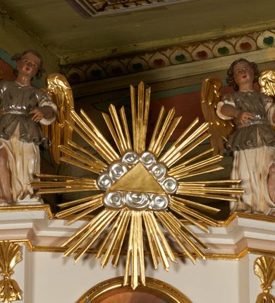 Zdjęcie nr 3: Nastawa architektoniczna, jednoosiowa, dwukondygnacyjna, ustawiona na niewielkim cokole, z dwoma prostopadłościennymi postumentami wydzielonymi po bokach. Ołtarz drewniany, prostopadłościenny, z drewnianą mensą. Antepedium w formie poziomego prostokąta ujętego profilowaną ramą, w polu malowany monogram IHS flankowany gałązkami lilii, u dołu girlanda kwiatowa. W predelli nastawy płycina w formie poziomego prostokąta poszerzonego na krótszych bokach za pomocą nadwieszonych łuków półkolistych, ze sceną modlitwy Chrystusa w Ogrójcu. Pierwsza kondygnacja ujęta parą kolumn stojących na postumentach, o skręconych trzonach dekorowanych ornamentem roślinnym. Podpory dźwigają belkowanie, o pełnych odcinkach nad kolumnami ustawionych pod kątem, z architrawem wyłamującym się schodkowo nad polem środkowym oraz gzymsem przyjmującym formę trzech boków z ośmioboku oraz przerwany, falisty przyczółek. Fryz belkowania ozdobiony jest ornamentem roślinnym, gzyms zaś dekorowany muszlą i zwisami kwiatowymi. Całe pole środkowe wypełnia nisza w kształcie stojącego prostokąta z wciętymi narożami, ujęta ramą ozdobioną ornamentem roślinnym, wewnątrz znajduje się rzeźbiarska grupa Ukrzyżowania na tle malowanego pejzażu. Pierwsza kondygnacja ujęta jest uszami utworzonymi z suchego akantu, w ich dolnej części postumenty dla figur św. Walentego i św. Jana Ewangelisty. Druga kondygnacja jest węższa od poprzedniej, flankowana parą ustawionych lekko pod kątem pilastrów dźwigających gzyms, dekorowanych w partii trzonów kampanulami. W polu obraz ze św. Wawrzyńcem w formie pionowego owalu w profilowanej ramie. Całość zwieńczona okiem Opatrzności na tle obłoków w glorii promienistej. Na belkowaniu niewielkie figury aniołów. Druga kondygnacja ujęta jest pionowymi rzędami kampanul. Struktura polichromowana w kolorze białym, z pozłacanymi profilami i elementami ornamentyki oraz srebrzonymi detalami. 