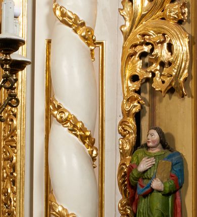 Zdjęcie nr 26: Nastawa architektoniczna, jednoosiowa, dwukondygnacyjna, ustawiona na niewielkim cokole, z dwoma prostopadłościennymi postumentami wydzielonymi po bokach. Ołtarz drewniany, prostopadłościenny, z drewnianą mensą. Antepedium w formie poziomego prostokąta ujętego profilowaną ramą, w polu malowany monogram IHS flankowany gałązkami lilii, u dołu girlanda kwiatowa. W predelli nastawy płycina w formie poziomego prostokąta poszerzonego na krótszych bokach za pomocą nadwieszonych łuków półkolistych, ze sceną modlitwy Chrystusa w Ogrójcu. Pierwsza kondygnacja ujęta parą kolumn stojących na postumentach, o skręconych trzonach dekorowanych ornamentem roślinnym. Podpory dźwigają belkowanie, o pełnych odcinkach nad kolumnami ustawionych pod kątem, z architrawem wyłamującym się schodkowo nad polem środkowym oraz gzymsem przyjmującym formę trzech boków z ośmioboku oraz przerwany, falisty przyczółek. Fryz belkowania ozdobiony jest ornamentem roślinnym, gzyms zaś dekorowany muszlą i zwisami kwiatowymi. Całe pole środkowe wypełnia nisza w kształcie stojącego prostokąta z wciętymi narożami, ujęta ramą ozdobioną ornamentem roślinnym, wewnątrz znajduje się rzeźbiarska grupa Ukrzyżowania na tle malowanego pejzażu. Pierwsza kondygnacja ujęta jest uszami utworzonymi z suchego akantu, w ich dolnej części postumenty dla figur św. Walentego i św. Jana Ewangelisty. Druga kondygnacja jest węższa od poprzedniej, flankowana parą ustawionych lekko pod kątem pilastrów dźwigających gzyms, dekorowanych w partii trzonów kampanulami. W polu obraz ze św. Wawrzyńcem w formie pionowego owalu w profilowanej ramie. Całość zwieńczona okiem Opatrzności na tle obłoków w glorii promienistej. Na belkowaniu niewielkie figury aniołów. Druga kondygnacja ujęta jest pionowymi rzędami kampanul. Struktura polichromowana w kolorze białym, z pozłacanymi profilami i elementami ornamentyki oraz srebrzonymi detalami. 