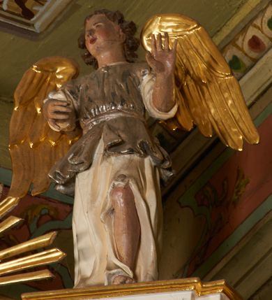 Zdjęcie nr 18: Nastawa architektoniczna, jednoosiowa, dwukondygnacyjna, ustawiona na niewielkim cokole, z dwoma prostopadłościennymi postumentami wydzielonymi po bokach. Ołtarz drewniany, prostopadłościenny, z drewnianą mensą. Antepedium w formie poziomego prostokąta ujętego profilowaną ramą, w polu malowany monogram IHS flankowany gałązkami lilii, u dołu girlanda kwiatowa. W predelli nastawy płycina w formie poziomego prostokąta poszerzonego na krótszych bokach za pomocą nadwieszonych łuków półkolistych, ze sceną modlitwy Chrystusa w Ogrójcu. Pierwsza kondygnacja ujęta parą kolumn stojących na postumentach, o skręconych trzonach dekorowanych ornamentem roślinnym. Podpory dźwigają belkowanie, o pełnych odcinkach nad kolumnami ustawionych pod kątem, z architrawem wyłamującym się schodkowo nad polem środkowym oraz gzymsem przyjmującym formę trzech boków z ośmioboku oraz przerwany, falisty przyczółek. Fryz belkowania ozdobiony jest ornamentem roślinnym, gzyms zaś dekorowany muszlą i zwisami kwiatowymi. Całe pole środkowe wypełnia nisza w kształcie stojącego prostokąta z wciętymi narożami, ujęta ramą ozdobioną ornamentem roślinnym, wewnątrz znajduje się rzeźbiarska grupa Ukrzyżowania na tle malowanego pejzażu. Pierwsza kondygnacja ujęta jest uszami utworzonymi z suchego akantu, w ich dolnej części postumenty dla figur św. Walentego i św. Jana Ewangelisty. Druga kondygnacja jest węższa od poprzedniej, flankowana parą ustawionych lekko pod kątem pilastrów dźwigających gzyms, dekorowanych w partii trzonów kampanulami. W polu obraz ze św. Wawrzyńcem w formie pionowego owalu w profilowanej ramie. Całość zwieńczona okiem Opatrzności na tle obłoków w glorii promienistej. Na belkowaniu niewielkie figury aniołów. Druga kondygnacja ujęta jest pionowymi rzędami kampanul. Struktura polichromowana w kolorze białym, z pozłacanymi profilami i elementami ornamentyki oraz srebrzonymi detalami. 