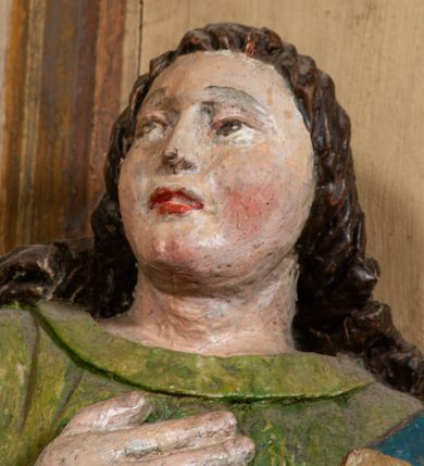 Zdjęcie nr 5: Rzeźba pełna, święty ustawiony jest frontalnie, w kontrapoście, z głową skierowaną w prawo, lewą ręką przyciska do boku księgę, prawą kładzie na piersi. Twarz świętego jest okrągła o dużych oczach skierowanych w bok, prostym nosie i pełnych ustach, okolona długimi, falowanymi włosami opadającymi na ramiona i plecy. Ubrany jest w zieloną suknię, przepasaną w talii i niebiesko-czerwony płaszcz zarzucony na lewe ramię, stopy świętego bose. Polichromia ciała traktowana naturalistycznie.