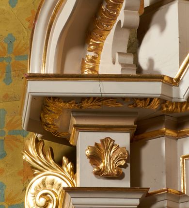 Zdjęcie nr 11: Nastawa ołtarzowa architektoniczna, jednoosiowa, dwukondygnacyjna, ustawiona na niewielkim cokole, z dwoma prostopadłościennymi postumentami wydzielonymi po bokach. Ołtarz drewniany, prostopadłościenny, z drewnianą mensą. Antepedium w formie poziomego prostokąta ujętego profilowaną ramą, w polu malowany monogram Marii, flankowany różanymi gałązkami. W predelli nastawy znajduje się płycina w formie poziomego prostokąta poszerzonego na krótszych bokach za pomocą nadwieszonych łuków półkolistych, ze sceną Zwiastowania. 
Pierwsza kondygnacja ujęta jest parą kolumn stojących na postumentach, o skręconych trzonach dekorowanych ornamentem roślinnym. Podpory dźwigają belkowanie, którego pełne odcinki nad kolumnami ustawione są pod kątem, architraw nad polem środkowym wyłamuje się schodkowo, a gzyms przyjmuje formę trzech boków z ośmioboku. Wyżej widoczny oraz przerwany falisty przyczółek. Fryz belkowania ozdobiony jest palmetami oraz dekoracją roślinną, gzyms dekorowany palmetą. Całe pole środkowe wypełnia obraz Matki Boskiej Różańcowej ze św. Dominikiem i św. Katarzyną Sieneńską w formie pionowego prostokąta z wciętymi narożami, w ramie ozdobionej stylizowanym ornamentem. Pierwsza kondygnacja ujęta jest częściowo ażurowymi uszami utworzonymi z akantu i karbowanej wstęgi. Druga kondygnacja jest węższa, flankowana parą ustawionych lekko pod kątem pilastrów, dekorowanych w partii trzonów kampanulami, dźwigających gzyms,. W polu obraz Objawienia Matki Boskiej w Lourdes w formie pionowego owalu w profilowanej ramie, flankowany kampanulami. Całość zwieńczona medalionem w glorii z monogramem Marii. Na belkowaniu niewielkie figury św. Barbary i św. Michała Archanioła. Druga kondygnacja ujęta jest pionowymi rzędami kampanul. Struktura polichromowana w kolorze białym z pozłacanymi profilami i elementami ornamentyki. 


