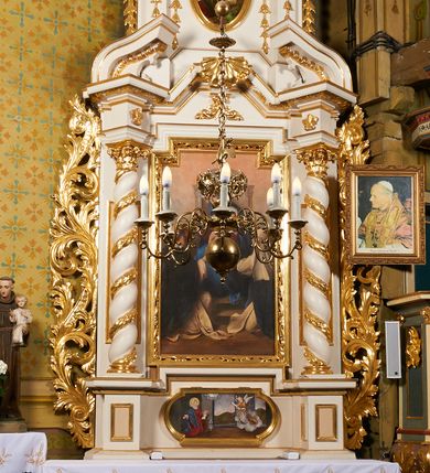 Zdjęcie nr 2: Nastawa ołtarzowa architektoniczna, jednoosiowa, dwukondygnacyjna, ustawiona na niewielkim cokole, z dwoma prostopadłościennymi postumentami wydzielonymi po bokach. Ołtarz drewniany, prostopadłościenny, z drewnianą mensą. Antepedium w formie poziomego prostokąta ujętego profilowaną ramą, w polu malowany monogram Marii, flankowany różanymi gałązkami. W predelli nastawy znajduje się płycina w formie poziomego prostokąta poszerzonego na krótszych bokach za pomocą nadwieszonych łuków półkolistych, ze sceną Zwiastowania. 
Pierwsza kondygnacja ujęta jest parą kolumn stojących na postumentach, o skręconych trzonach dekorowanych ornamentem roślinnym. Podpory dźwigają belkowanie, którego pełne odcinki nad kolumnami ustawione są pod kątem, architraw nad polem środkowym wyłamuje się schodkowo, a gzyms przyjmuje formę trzech boków z ośmioboku. Wyżej widoczny oraz przerwany falisty przyczółek. Fryz belkowania ozdobiony jest palmetami oraz dekoracją roślinną, gzyms dekorowany palmetą. Całe pole środkowe wypełnia obraz Matki Boskiej Różańcowej ze św. Dominikiem i św. Katarzyną Sieneńską w formie pionowego prostokąta z wciętymi narożami, w ramie ozdobionej stylizowanym ornamentem. Pierwsza kondygnacja ujęta jest częściowo ażurowymi uszami utworzonymi z akantu i karbowanej wstęgi. Druga kondygnacja jest węższa, flankowana parą ustawionych lekko pod kątem pilastrów, dekorowanych w partii trzonów kampanulami, dźwigających gzyms,. W polu obraz Objawienia Matki Boskiej w Lourdes w formie pionowego owalu w profilowanej ramie, flankowany kampanulami. Całość zwieńczona medalionem w glorii z monogramem Marii. Na belkowaniu niewielkie figury św. Barbary i św. Michała Archanioła. Druga kondygnacja ujęta jest pionowymi rzędami kampanul. Struktura polichromowana w kolorze białym z pozłacanymi profilami i elementami ornamentyki. 


