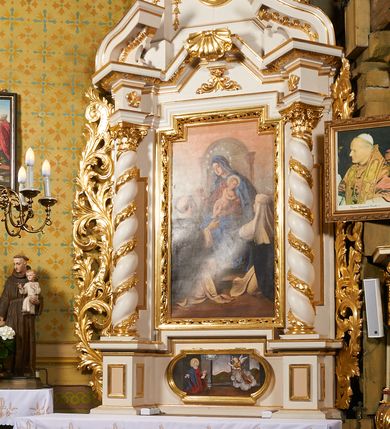 Zdjęcie nr 7: Nastawa ołtarzowa architektoniczna, jednoosiowa, dwukondygnacyjna, ustawiona na niewielkim cokole, z dwoma prostopadłościennymi postumentami wydzielonymi po bokach. Ołtarz drewniany, prostopadłościenny, z drewnianą mensą. Antepedium w formie poziomego prostokąta ujętego profilowaną ramą, w polu malowany monogram Marii, flankowany różanymi gałązkami. W predelli nastawy znajduje się płycina w formie poziomego prostokąta poszerzonego na krótszych bokach za pomocą nadwieszonych łuków półkolistych, ze sceną Zwiastowania. 
Pierwsza kondygnacja ujęta jest parą kolumn stojących na postumentach, o skręconych trzonach dekorowanych ornamentem roślinnym. Podpory dźwigają belkowanie, którego pełne odcinki nad kolumnami ustawione są pod kątem, architraw nad polem środkowym wyłamuje się schodkowo, a gzyms przyjmuje formę trzech boków z ośmioboku. Wyżej widoczny oraz przerwany falisty przyczółek. Fryz belkowania ozdobiony jest palmetami oraz dekoracją roślinną, gzyms dekorowany palmetą. Całe pole środkowe wypełnia obraz Matki Boskiej Różańcowej ze św. Dominikiem i św. Katarzyną Sieneńską w formie pionowego prostokąta z wciętymi narożami, w ramie ozdobionej stylizowanym ornamentem. Pierwsza kondygnacja ujęta jest częściowo ażurowymi uszami utworzonymi z akantu i karbowanej wstęgi. Druga kondygnacja jest węższa, flankowana parą ustawionych lekko pod kątem pilastrów, dekorowanych w partii trzonów kampanulami, dźwigających gzyms,. W polu obraz Objawienia Matki Boskiej w Lourdes w formie pionowego owalu w profilowanej ramie, flankowany kampanulami. Całość zwieńczona medalionem w glorii z monogramem Marii. Na belkowaniu niewielkie figury św. Barbary i św. Michała Archanioła. Druga kondygnacja ujęta jest pionowymi rzędami kampanul. Struktura polichromowana w kolorze białym z pozłacanymi profilami i elementami ornamentyki. 


