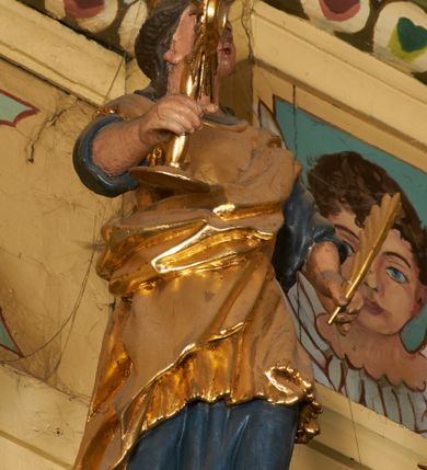 Zdjęcie nr 3: Postać ukazana jest frontalnie, z głową skierowaną delikatnie w lewo, w lewej ręce trzyma liść palmy, w prawej monstrancję. Święta ma okrągłą twarz o pełnych policzkach, okoloną długimi włosami spiętymi z tyłu głowy i opadającymi na plecy. Ubrana jest w długą, niebieską suknię spodnią, pozłacaną suknię wierzchnią sięgającą kolan, przepasaną w talii oraz pozłacany płaszcz przewiązany diagonalnie przez lewe ramię. Na głowie ma koronę. Polichromia naturalistyczna, część szat i atrybuty pozłacane.
