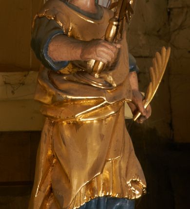 Zdjęcie nr 4: Postać ukazana jest frontalnie, z głową skierowaną delikatnie w lewo, w lewej ręce trzyma liść palmy, w prawej monstrancję. Święta ma okrągłą twarz o pełnych policzkach, okoloną długimi włosami spiętymi z tyłu głowy i opadającymi na plecy. Ubrana jest w długą, niebieską suknię spodnią, pozłacaną suknię wierzchnią sięgającą kolan, przepasaną w talii oraz pozłacany płaszcz przewiązany diagonalnie przez lewe ramię. Na głowie ma koronę. Polichromia naturalistyczna, część szat i atrybuty pozłacane.
