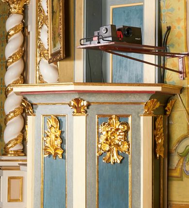 Zdjęcie nr 10: Ambona jest przyścienna, wisząca, z dostępem od zakrystii przez drzwiczki w zaplecku. Kosz ma na planie połowy ośmioboku, na podstawie w formie wałka dekorowanego liśćmi, z podwieszeniem zakończonym szyszką. Ścianki kosza wydzielone są pilastrami rozmieszczonymi w narożach wieloboku, zakończonymi palmetami. Pomiędzy pilastrami znajdują się prostokątne płyciny dekorowane w górnej części ornamentem roślinnym, parapet przyjmuje formę gzymsu. Rolę zaplecka pełnią prostokątne drzwi we wnęce ujęte prostą ramą. Baldachim niepołączony z zapleckiem, na planie ośmioboku, ma formę pełnego belkowania dekorowanego kostkowaniem, w partii fryzu widnieje napis: „A(NNO) D(OMINI) 1601. [CUSTO]DIVNT ILLV[D] VERBVM DEI. BEATI QUI”. Podniebienie baldachimu malowane jest w motywy roślinne z podwieszoną rzeźbioną gołębicą Ducha Świętego w glorii promienistej. Struktura polichromowana jest w kolorze błękitnym, szarym i kremowym, z czerwonymi, pozłacanymi i posrebrzanymi elementami. 

