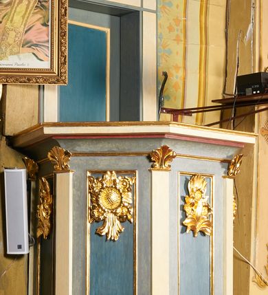 Zdjęcie nr 12: Ambona jest przyścienna, wisząca, z dostępem od zakrystii przez drzwiczki w zaplecku. Kosz ma na planie połowy ośmioboku, na podstawie w formie wałka dekorowanego liśćmi, z podwieszeniem zakończonym szyszką. Ścianki kosza wydzielone są pilastrami rozmieszczonymi w narożach wieloboku, zakończonymi palmetami. Pomiędzy pilastrami znajdują się prostokątne płyciny dekorowane w górnej części ornamentem roślinnym, parapet przyjmuje formę gzymsu. Rolę zaplecka pełnią prostokątne drzwi we wnęce ujęte prostą ramą. Baldachim niepołączony z zapleckiem, na planie ośmioboku, ma formę pełnego belkowania dekorowanego kostkowaniem, w partii fryzu widnieje napis: „A(NNO) D(OMINI) 1601. [CUSTO]DIVNT ILLV[D] VERBVM DEI. BEATI QUI”. Podniebienie baldachimu malowane jest w motywy roślinne z podwieszoną rzeźbioną gołębicą Ducha Świętego w glorii promienistej. Struktura polichromowana jest w kolorze błękitnym, szarym i kremowym, z czerwonymi, pozłacanymi i posrebrzanymi elementami. 

