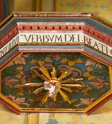 Zdjęcie nr 13: Ambona jest przyścienna, wisząca, z dostępem od zakrystii przez drzwiczki w zaplecku. Kosz ma na planie połowy ośmioboku, na podstawie w formie wałka dekorowanego liśćmi, z podwieszeniem zakończonym szyszką. Ścianki kosza wydzielone są pilastrami rozmieszczonymi w narożach wieloboku, zakończonymi palmetami. Pomiędzy pilastrami znajdują się prostokątne płyciny dekorowane w górnej części ornamentem roślinnym, parapet przyjmuje formę gzymsu. Rolę zaplecka pełnią prostokątne drzwi we wnęce ujęte prostą ramą. Baldachim niepołączony z zapleckiem, na planie ośmioboku, ma formę pełnego belkowania dekorowanego kostkowaniem, w partii fryzu widnieje napis: „A(NNO) D(OMINI) 1601. [CUSTO]DIVNT ILLV[D] VERBVM DEI. BEATI QUI”. Podniebienie baldachimu malowane jest w motywy roślinne z podwieszoną rzeźbioną gołębicą Ducha Świętego w glorii promienistej. Struktura polichromowana jest w kolorze błękitnym, szarym i kremowym, z czerwonymi, pozłacanymi i posrebrzanymi elementami. 

