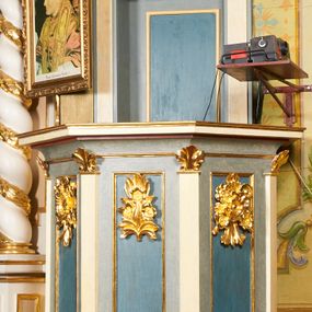 Zdjęcie nr 1: Ambona jest przyścienna, wisząca, z dostępem od zakrystii przez drzwiczki w zaplecku. Kosz ma na planie połowy ośmioboku, na podstawie w formie wałka dekorowanego liśćmi, z podwieszeniem zakończonym szyszką. Ścianki kosza wydzielone są pilastrami rozmieszczonymi w narożach wieloboku, zakończonymi palmetami. Pomiędzy pilastrami znajdują się prostokątne płyciny dekorowane w górnej części ornamentem roślinnym, parapet przyjmuje formę gzymsu. Rolę zaplecka pełnią prostokątne drzwi we wnęce ujęte prostą ramą. Baldachim niepołączony z zapleckiem, na planie ośmioboku, ma formę pełnego belkowania dekorowanego kostkowaniem, w partii fryzu widnieje napis: „A(NNO) D(OMINI) 1601. [CUSTO]DIVNT ILLV[D] VERBVM DEI. BEATI QUI”. Podniebienie baldachimu malowane jest w motywy roślinne z podwieszoną rzeźbioną gołębicą Ducha Świętego w glorii promienistej. Struktura polichromowana jest w kolorze błękitnym, szarym i kremowym, z czerwonymi, pozłacanymi i posrebrzanymi elementami. 

