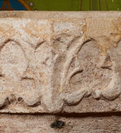 Zdjęcie nr 11: Kamienna chrzcielnica stoi na niewysokiej, kamiennej podstawie na planie koła. Jej stopa jest na planie ośmioboku, u dołu z pionowo ściętym cokołem i zwęża się stożkowato ku górze. Nodus jest spłaszczony, ośmioboczny. Czara ośmioboczna, dwustrefowa, u dołu zaokrąglona, u góry prosto ścięta, nadwieszona, w górnej strefie pola dekorowane są motywem trójlistnego maswerku. Wewnątrz czary znajduje się metalowa misa. Drewniana pokrywa przyjmuje kształt korony zamkniętej sześcioma kabłąkami z kulą i krzyżem umieszczonymi na szczycie. Polichromowana w kolorach zielonym i czerwonym, wewnątrz na niebiesko, obręcz korony i kula posrebrzane, detale i brzegi pozłacane.