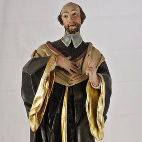 Zdjęcie nr 1: Rzeźba św. Jana Kantego jest z tyłu drążona, ustawiona na dwustrefowym cokole, który stanowią skrzynki na relikwie z wyciętymi z przodu otworami. Święty ukazany jest w całej postaci, frontalnie, stoi w kontrapoście. Prawą dłoń kładzie na piersi, lewa jest uniesiona w geście błogosławieństwa. Twarz świętego jest szczupła, o wysokim czole, dużym i szerokim nosie, półkoliście zarysowanych łukach brwiowych, migdałowatych oczach oraz pełnych, delikatnie rozchylonych ustach. Okolona jest kręconą brodą i krótkimi brązowymi włosami skręconymi w pukle po bokach głowy z łysiną. Święty ubrany jest w czarną sutannę zapinaną na guziki z błękitną befką (krawat w formie dwóch rozdzielonych pasów) oraz rozchyloną z przodu czarną togę profesorską o szerokich rękawach z pozłacaną podszewką i kołnierzem. Figura w partiach ciała polichromowana naturalistycznie.
