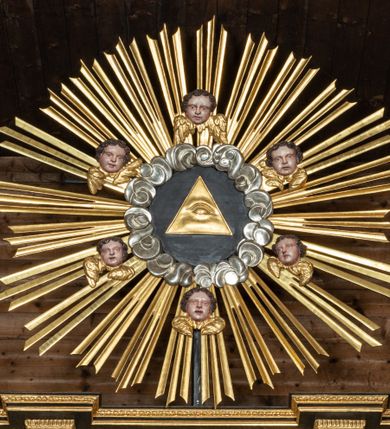 Zdjęcie nr 19: Ołtarz przyścienny, architektoniczny, trójosiowy, dwukondygnacjowy. Nastawa ołtarzowa ustawiona na prostopadłościennym stole ołtarzowym, zasłanym czerwonym materiałem. Predella na niskim cokoliku w formie półwałku, zamknięta u góry puklowanym gzymsem. W osi środkowej wmontowane tabernakulum ozdobione bujną, płaskorzeźbioną winną latoroślą. Po jego bokach ścianki z lustrami, flankowane parą spiralnie skręconych laskowań. W osiach bocznych predelli płyciny o uszatych narożach, w polu których znajdują się pilastry hermowe ze skierowanymi na wprost kobiecymi głowami. Na skrajach predelli konsolki, bogato dekorowane wicią, zawijającą się w wolutki, zdobioną perełkowaniem; na brzegu konsolki skierowana ku dołowi głowa. Pierwsza kondygnacja artykułowana parą kolumn o korynckich kapitelach, wspierających niepełne belkowanie, wyłamane na ich osi. W polu głównym obraz Matki Boskiej z Dzieciątkiem, w osiach bocznych wmontowane skrzydła tryptyku z przedstawieniami: Ecce Homo po lewej stronie oraz Matki Boskiej Bolesnej po prawej stronie. Każda z osi ujęta na brzegach obramowaniem w kształcie stojącego prostokąta o uszatych narożnikach. Fryz dekorowany symetryczną wicią roślinną, nad kolumnami srebrzone rauty. Druga kondygnacja mniejsza, flankowana analogicznymi kolumnami, wspierającymi podobne belkowanie. W polu głównym obraz św. Andrzeja w kształcie stojącego prostokąta. W lewej osi bocznej obraz św. Wojciecha, a w prawej św. Stanisława, oba zamknięte łukiem nadwieszonym. Po bokach kondygnacji uszy o wykroju okuciowym, zdobione wicią oraz podwieszonymi girlandami z owocami winogron. Nad ołtarzem zamocowana promienista gloria, w polu której znajduje się oko Opatrzności otoczone wieńcem z obłoków oraz sześcioma skrzydlatymi główkami anielskimi. Struktura malowana na kolor czarny, kolumny i ornamentyka złocone, detale srebrzone.