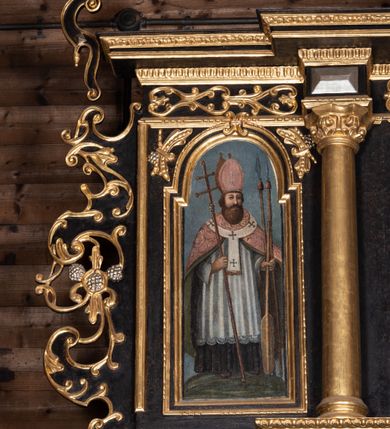 Zdjęcie nr 8: Ołtarz przyścienny, architektoniczny, trójosiowy, dwukondygnacjowy. Nastawa ołtarzowa ustawiona na prostopadłościennym stole ołtarzowym, zasłanym czerwonym materiałem. Predella na niskim cokoliku w formie półwałku, zamknięta u góry puklowanym gzymsem. W osi środkowej wmontowane tabernakulum ozdobione bujną, płaskorzeźbioną winną latoroślą. Po jego bokach ścianki z lustrami, flankowane parą spiralnie skręconych laskowań. W osiach bocznych predelli płyciny o uszatych narożach, w polu których znajdują się pilastry hermowe ze skierowanymi na wprost kobiecymi głowami. Na skrajach predelli konsolki, bogato dekorowane wicią, zawijającą się w wolutki, zdobioną perełkowaniem; na brzegu konsolki skierowana ku dołowi głowa. Pierwsza kondygnacja artykułowana parą kolumn o korynckich kapitelach, wspierających niepełne belkowanie, wyłamane na ich osi. W polu głównym obraz Matki Boskiej z Dzieciątkiem, w osiach bocznych wmontowane skrzydła tryptyku z przedstawieniami: Ecce Homo po lewej stronie oraz Matki Boskiej Bolesnej po prawej stronie. Każda z osi ujęta na brzegach obramowaniem w kształcie stojącego prostokąta o uszatych narożnikach. Fryz dekorowany symetryczną wicią roślinną, nad kolumnami srebrzone rauty. Druga kondygnacja mniejsza, flankowana analogicznymi kolumnami, wspierającymi podobne belkowanie. W polu głównym obraz św. Andrzeja w kształcie stojącego prostokąta. W lewej osi bocznej obraz św. Wojciecha, a w prawej św. Stanisława, oba zamknięte łukiem nadwieszonym. Po bokach kondygnacji uszy o wykroju okuciowym, zdobione wicią oraz podwieszonymi girlandami z owocami winogron. Nad ołtarzem zamocowana promienista gloria, w polu której znajduje się oko Opatrzności otoczone wieńcem z obłoków oraz sześcioma skrzydlatymi główkami anielskimi. Struktura malowana na kolor czarny, kolumny i ornamentyka złocone, detale srebrzone.