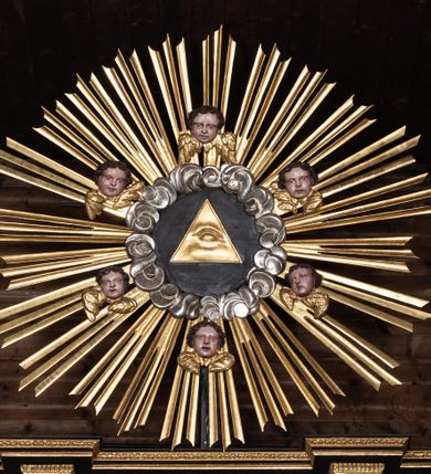 Zdjęcie nr 20: Ołtarz przyścienny, architektoniczny, trójosiowy, dwukondygnacjowy. Nastawa ołtarzowa ustawiona na prostopadłościennym stole ołtarzowym, zasłanym czerwonym materiałem. Predella na niskim cokoliku w formie półwałku, zamknięta u góry puklowanym gzymsem. W osi środkowej wmontowane tabernakulum ozdobione bujną, płaskorzeźbioną winną latoroślą. Po jego bokach ścianki z lustrami, flankowane parą spiralnie skręconych laskowań. W osiach bocznych predelli płyciny o uszatych narożach, w polu których znajdują się pilastry hermowe ze skierowanymi na wprost kobiecymi głowami. Na skrajach predelli konsolki, bogato dekorowane wicią, zawijającą się w wolutki, zdobioną perełkowaniem; na brzegu konsolki skierowana ku dołowi głowa. Pierwsza kondygnacja artykułowana parą kolumn o korynckich kapitelach, wspierających niepełne belkowanie, wyłamane na ich osi. W polu głównym obraz Matki Boskiej z Dzieciątkiem, w osiach bocznych wmontowane skrzydła tryptyku z przedstawieniami: Ecce Homo po lewej stronie oraz Matki Boskiej Bolesnej po prawej stronie. Każda z osi ujęta na brzegach obramowaniem w kształcie stojącego prostokąta o uszatych narożnikach. Fryz dekorowany symetryczną wicią roślinną, nad kolumnami srebrzone rauty. Druga kondygnacja mniejsza, flankowana analogicznymi kolumnami, wspierającymi podobne belkowanie. W polu głównym obraz św. Andrzeja w kształcie stojącego prostokąta. W lewej osi bocznej obraz św. Wojciecha, a w prawej św. Stanisława, oba zamknięte łukiem nadwieszonym. Po bokach kondygnacji uszy o wykroju okuciowym, zdobione wicią oraz podwieszonymi girlandami z owocami winogron. Nad ołtarzem zamocowana promienista gloria, w polu której znajduje się oko Opatrzności otoczone wieńcem z obłoków oraz sześcioma skrzydlatymi główkami anielskimi. Struktura malowana na kolor czarny, kolumny i ornamentyka złocone, detale srebrzone.