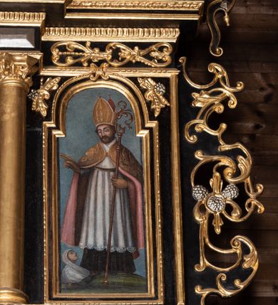 Zdjęcie nr 12: Ołtarz przyścienny, architektoniczny, trójosiowy, dwukondygnacjowy. Nastawa ołtarzowa ustawiona na prostopadłościennym stole ołtarzowym, zasłanym czerwonym materiałem. Predella na niskim cokoliku w formie półwałku, zamknięta u góry puklowanym gzymsem. W osi środkowej wmontowane tabernakulum ozdobione bujną, płaskorzeźbioną winną latoroślą. Po jego bokach ścianki z lustrami, flankowane parą spiralnie skręconych laskowań. W osiach bocznych predelli płyciny o uszatych narożach, w polu których znajdują się pilastry hermowe ze skierowanymi na wprost kobiecymi głowami. Na skrajach predelli konsolki, bogato dekorowane wicią, zawijającą się w wolutki, zdobioną perełkowaniem; na brzegu konsolki skierowana ku dołowi głowa. Pierwsza kondygnacja artykułowana parą kolumn o korynckich kapitelach, wspierających niepełne belkowanie, wyłamane na ich osi. W polu głównym obraz Matki Boskiej z Dzieciątkiem, w osiach bocznych wmontowane skrzydła tryptyku z przedstawieniami: Ecce Homo po lewej stronie oraz Matki Boskiej Bolesnej po prawej stronie. Każda z osi ujęta na brzegach obramowaniem w kształcie stojącego prostokąta o uszatych narożnikach. Fryz dekorowany symetryczną wicią roślinną, nad kolumnami srebrzone rauty. Druga kondygnacja mniejsza, flankowana analogicznymi kolumnami, wspierającymi podobne belkowanie. W polu głównym obraz św. Andrzeja w kształcie stojącego prostokąta. W lewej osi bocznej obraz św. Wojciecha, a w prawej św. Stanisława, oba zamknięte łukiem nadwieszonym. Po bokach kondygnacji uszy o wykroju okuciowym, zdobione wicią oraz podwieszonymi girlandami z owocami winogron. Nad ołtarzem zamocowana promienista gloria, w polu której znajduje się oko Opatrzności otoczone wieńcem z obłoków oraz sześcioma skrzydlatymi główkami anielskimi. Struktura malowana na kolor czarny, kolumny i ornamentyka złocone, detale srebrzone.