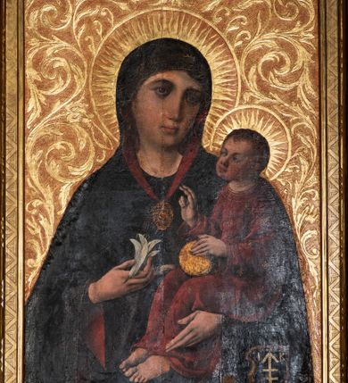 Zdjęcie nr 2: Obraz w kształcie stojącego prostokąta. W centrum kompozycji Matka Boska w typie Hodegetrii ukazana w półpostaci, frontalnie z Dzieciątkiem Jezus na lewym ręku i kwiatem białej lilii w prawej dłoni. Twarz Marii szeroka, z długim nosem, małymi ustami, ciemnobrązowymi oczami. Ubrana jest w ciemnoniebieską suknię oraz ciemnoniebieski płaszcz z czerwoną podszewką i złotą lamówką na brzegu, zarzucony na ramiona i głowę, spięty na piersi złotą, owalną broszką, zdobioną w okuciowe motywy. Dzieciątko ukazane w całej postaci, zwrócone trzy czwarte w prawo, lewą ręką przytrzymuje złote jabłko królewskie, prawą unosi na wysokości piersi w geście błogosławieństwa. Twarz okrągła z długim i szerokim nosem, wąskimi ustami, okolona krótkimi i brązowymi włosami. Jezus ubrany jest w czerwoną suknię z długimi rękawami, zdobioną złotymi rozetkami. Głowy obu postaci ujmują złocone promieniste nimby, otoczone złotym okręgiem. W prawym dolnym narożu obrazu tarcza z godłem herbu Lis oraz sygle „IK”. Tło złote, ryte w ornamenty roślinne. 
