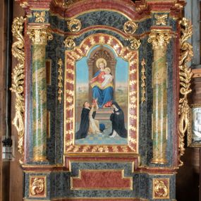 Zdjęcie nr 1: Ołtarz przyścienny, architektoniczny, jednokondygnacyjny, jednoosiowy ze zwieńczeniem. Mensa prostopadłościenna, drewniana, ustawiona na cokole, zamknięta profilowanym gzymsem. Antepedium zdobione malowaną płyciną w kształcie leżącego prostokąta o wklęsłych narożach i zryzalitowanym górnym i dolnym boku. W polu monogram IHS otoczony wieńcem z kłosów zbóż. Tło jasnoniebieskie, fakturowane w ciemnoszare plamki. Nastawa ołtarzowa ustawiona na niskim cokole o wysuniętych do przodu impostach, na których ustawiona jest para kolumn, wspierających przerwane belkowanie i wolutowy przyczółek. Pośrodku w ramie ozdobionej płaskorzeźbionymi liśćmi obraz Matki Boskiej Różańcowej w kształcie stojącego prostokąta, zamkniętego łukiem wklęsło-wypukłym z uskokami. Po bokach obrazu zwisy z kamapnul. Fryz dekorowany liśćmi akantu i rozetkami. Na tle kolumn prostokątne płyciny. W zwieńczeniu monogram maryjny na tle promienistej glorii z czterema uskrzydlonymi główkami anielskimi. Po bokach ołtarza akantowe uszy, przeplecione karbowaną wstęgą. Imposty w partii cokołu zdobione płycinami w kształcie niewielkich prostokątów, wypełnionych liśćmi akantu. Struktura malowana na kolor ciemnoniebieski i fakturowana w szare plamki, trzony kolumn marmoryzowane na kolor zielono-beżowy, profilowania na kolor bordowy, detale i ornamentyka złocone. 