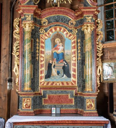 Zdjęcie nr 2: Ołtarz przyścienny, architektoniczny, jednokondygnacyjny, jednoosiowy ze zwieńczeniem. Mensa prostopadłościenna, drewniana, ustawiona na cokole, zamknięta profilowanym gzymsem. Antepedium zdobione malowaną płyciną w kształcie leżącego prostokąta o wklęsłych narożach i zryzalitowanym górnym i dolnym boku. W polu monogram IHS otoczony wieńcem z kłosów zbóż. Tło jasnoniebieskie, fakturowane w ciemnoszare plamki. Nastawa ołtarzowa ustawiona na niskim cokole o wysuniętych do przodu impostach, na których ustawiona jest para kolumn, wspierających przerwane belkowanie i wolutowy przyczółek. Pośrodku w ramie ozdobionej płaskorzeźbionymi liśćmi obraz Matki Boskiej Różańcowej w kształcie stojącego prostokąta, zamkniętego łukiem wklęsło-wypukłym z uskokami. Po bokach obrazu zwisy z kamapnul. Fryz dekorowany liśćmi akantu i rozetkami. Na tle kolumn prostokątne płyciny. W zwieńczeniu monogram maryjny na tle promienistej glorii z czterema uskrzydlonymi główkami anielskimi. Po bokach ołtarza akantowe uszy, przeplecione karbowaną wstęgą. Imposty w partii cokołu zdobione płycinami w kształcie niewielkich prostokątów, wypełnionych liśćmi akantu. Struktura malowana na kolor ciemnoniebieski i fakturowana w szare plamki, trzony kolumn marmoryzowane na kolor zielono-beżowy, profilowania na kolor bordowy, detale i ornamentyka złocone. 