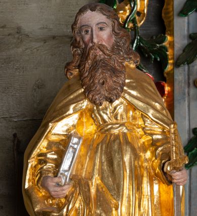 Zdjęcie nr 1: Rzeźba ścięta z tyłu została ustawiona na podstawie w formie kostki o ściętych narożach. Figura jest zwrócona frontalnie, w delikatnym kontrapoście. Święty prawą ręką przytrzymuje przy boku księgę, w lewej, ugiętej rękojeść miecza skierowanego ostrzem w dół. Twarz ma pociągłą, szczupłą, o głęboko osadzonych oczach, długim, prostym nosie; okoloną długą, falowaną brodą opadającą na pierś. Włosy ma długie, gęste, kręcone, z przedziałkiem na środku głowy, opadające na ramiona i plecy. Ubrany jest w złotą tunikę z długimi, wąskimi rękawami, przewiązaną wysoko w talii, drapowaną w liczne, równoległe fałdki oraz złoty płaszcz zapięty na piersi, opadający na ramiona i podtrzymywany prawą ręką na boku, drapowany i marszczony. Polichromia naturalistyczna w odsłoniętych partiach ciała, atrybuty złocone i srebrzone.