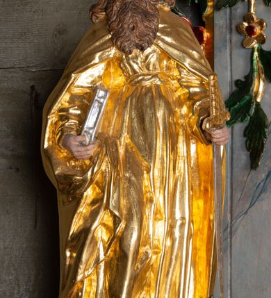 Zdjęcie nr 2: Rzeźba ścięta z tyłu została ustawiona na podstawie w formie kostki o ściętych narożach. Figura jest zwrócona frontalnie, w delikatnym kontrapoście. Święty prawą ręką przytrzymuje przy boku księgę, w lewej, ugiętej rękojeść miecza skierowanego ostrzem w dół. Twarz ma pociągłą, szczupłą, o głęboko osadzonych oczach, długim, prostym nosie; okoloną długą, falowaną brodą opadającą na pierś. Włosy ma długie, gęste, kręcone, z przedziałkiem na środku głowy, opadające na ramiona i plecy. Ubrany jest w złotą tunikę z długimi, wąskimi rękawami, przewiązaną wysoko w talii, drapowaną w liczne, równoległe fałdki oraz złoty płaszcz zapięty na piersi, opadający na ramiona i podtrzymywany prawą ręką na boku, drapowany i marszczony. Polichromia naturalistyczna w odsłoniętych partiach ciała, atrybuty złocone i srebrzone.