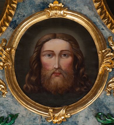 Zdjęcie nr 8: Nastawa ołtarzowa drewniana, architektoniczna, jednoosiowa, jednokondygnacyjna ze zwieńczeniem. Mensa w typie sarkofagowym, wklęsło-wypukła, zwężający się ku dołowi, zamknięta gzymsem; naroża ujęte fragmentami rocaille&#039;u, na froncie rocaille’owy kartusz; portatyl kamienny. Retabulum posadowione na cokole zryzalitowanym po bokach, zamkniętym silnie wysuniętym gzymsem; ujęte parą kolumn o kapitelach korynckich dźwigających imposty, których fryz przebiega przez całą szerokość retabulum, przyjmując nad polem środkowym formę łuku półkolistego nadwieszonego. W polu środkowym znajduje się nisza w formie kwadratu zamkniętego łukiem półkolistym nadwieszonym z płaskorzeźbioną sceną Świętej Rodziny w warsztacie, ujętego trzema ramami. Zwieńczenie ma formę zbliżoną do trapezu. Jest flankowane spływami wolutowymi i zamknięte baldachimem z profilowanym cokołem. W polu medalion otoczony profilowaną ramą z obrazem „Veraikon”. Cokoły kolumn dekorowane z trzech stron płycinami z ornamentem roślinnym; w polu predelli płycina w formie leżącego prostokąta o wypukłych ściankach bocznych z ornamentem roślinnym. Kondygnacja ujęta uszami utworzonymi z mięsistego akantu. Na fryzie rozety; na impostach rokokowe wazony z dużymi kwiatami słonecznika, róż i lilii, rama obrazu zwieńczenia dekorowana ornamentem roślinnym; u spodu akant z rozetami. Baldachim z podwieszonym lambrekinem; na jego cokole rokokowy wazon z dużymi kwiatami słonecznika, róż i lilii. Struktura marmoryzowana w kolorze szaro-niebieskim; ornamentyka, profile i kolumny złocone i srebrzone.