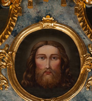 Zdjęcie nr 7: Nastawa ołtarzowa drewniana, architektoniczna, jednoosiowa, jednokondygnacyjna ze zwieńczeniem. Mensa w typie sarkofagowym, wklęsło-wypukła, zwężający się ku dołowi, zamknięta gzymsem; naroża ujęte fragmentami rocaille'u, na froncie rocaille’owy kartusz; portatyl kamienny. Retabulum posadowione na cokole zryzalitowanym po bokach, zamkniętym silnie wysuniętym gzymsem; ujęte parą kolumn o kapitelach korynckich dźwigających imposty, których fryz przebiega przez całą szerokość retabulum, przyjmując nad polem środkowym formę łuku półkolistego nadwieszonego. W polu środkowym znajduje się nisza w formie kwadratu zamkniętego łukiem półkolistym nadwieszonym z płaskorzeźbioną sceną Świętej Rodziny w warsztacie, ujętego trzema ramami. Zwieńczenie ma formę zbliżoną do trapezu. Jest flankowane spływami wolutowymi i zamknięte baldachimem z profilowanym cokołem. W polu medalion otoczony profilowaną ramą z obrazem „Veraikon”. Cokoły kolumn dekorowane z trzech stron płycinami z ornamentem roślinnym; w polu predelli płycina w formie leżącego prostokąta o wypukłych ściankach bocznych z ornamentem roślinnym. Kondygnacja ujęta uszami utworzonymi z mięsistego akantu. Na fryzie rozety; na impostach rokokowe wazony z dużymi kwiatami słonecznika, róż i lilii, rama obrazu zwieńczenia dekorowana ornamentem roślinnym; u spodu akant z rozetami. Baldachim z podwieszonym lambrekinem; na jego cokole rokokowy wazon z dużymi kwiatami słonecznika, róż i lilii. Struktura marmoryzowana w kolorze szaro-niebieskim; ornamentyka, profile i kolumny złocone i srebrzone.