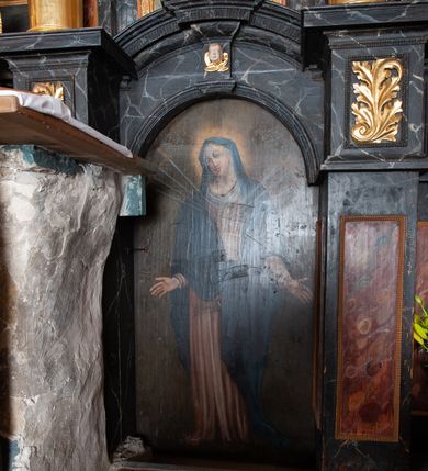 Zdjęcie nr 16: Ołtarz trójosiowy, dwukondygnacyjny z bramkami o formach architektonicznych, uszaty. Mensa murowana, prostopadłościenna z drewnianym antepedium ujętym profilowaną ramą z malowaną dekoracją roślinną. W polu malowane na płótnie przedstawienie adoracji Najświętszego Sakramentu. Tabernakulum w formie prostopadłościanu, o wypukłej ściance frontowej, ujętej pilastrami o kapitelach w formie akantowych konsol podtrzymujących pełne belkowanie. Na trzonach owalne lustra w akantowych ramach. W zwieńczeniu dwie uskrzydlone główki anielskie. Na metalowych drzwiczkach krucyfiks oraz kielich z hostią w otoczeniu winnych gron i kłosów (na odwrociu). Naroża tabernakulum flankuje para aniołów ustawionych na wolutowych konsolach. Nastawa umieszczona na wysokim cokole z bramkami mieszczącymi obrazy Chrystusa w typie Ecce Homo (z lewej) oraz Matki Boskiej Bolesnej (z prawej). Cokół artykułowany wysokimi postumentami, na których ustawione są kolumny. W polach postumentów złocona dekoracja akantowa. Kondygnacja pierwsza trójosiowa, artykułowana złoconymi kolumnami o korynckich kapitelach, ujęta srebrzonymi akantowymi uszami (suchy akant). Kolumny dźwigają pełne belkowanie, wyłamane na osiach podpór oraz odcinki przyczółka, na których siedzą figury aniołów w białych szatach. Dodatkowo, w osiach kolumn umieszczone mniejsze figury klęczących aniołów (osie wewnętrzne) oraz marmoryzowane, owalne kartusze ujęte złoconymi ramami z ornamentem małżowinowo-chrząstkowym (osie zewnętrzne). W partii fryzu złocone rozetki oraz marmoryzowane, owalne kartusze ujęte złoconym akantem. Gzyms profilowany, dekorowany dodatkowo złoconym kimationem. W polu środkowym prostokątny obraz przedstawiający Rodzinę Marii. Na zasuwie umieszczony obraz z wizerunkiem św. Katarzyny Aleksandryjskiej. Powyżej, w osi ołtarza obraz ze sceną Koronacji Marii, o nieregularnym kształcie w akantowej ramie, zwieńczonej koroną. W osiach bocznych umieszczone skrzydła boczne dawnego, gotyckiego tryptyku z wizerunkami św. Jana Chrzciciela i św. Barbary (z lewej) oraz św. Stanisława biskupa i św. Katarzyny Aleksandryjskiej (z prawej). Zwieńczenie ołtarza w formie edikuli ujętej złoconymi, korynckimi kolumnami oraz złoconymi, akantowymi uszami. Po bokach niewielkie figury klęczących aniołów. Podpory dźwigają wyłamane belkowanie dekorowane kimationem i rozetkami, łukowato wyginające się w osi ołtarza. W polu obraz w kształcie stojącego prostokąta zamkniętego łukiem półkolistym ze sceną Zwiastowania. Całość zwieńczona srebrzonym baldachimem z podwieszonej tkaniny przewiązanej złotym sznurem ze złoconą koroną umieszczoną na szczycie. Struktura ołtarza marmoryzowana w odcieniu ciemnoszarym, profile i płyciny na filarach marmoryzowane w kolorze bordowym, ornamentyka złocona i posrebrzana.