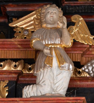 Zdjęcie nr 14: Ołtarz trójosiowy, dwukondygnacyjny z bramkami o formach architektonicznych, uszaty. Mensa murowana, prostopadłościenna z drewnianym antepedium ujętym profilowaną ramą z malowaną dekoracją roślinną. W polu malowane na płótnie przedstawienie adoracji Najświętszego Sakramentu. Tabernakulum w formie prostopadłościanu, o wypukłej ściance frontowej, ujętej pilastrami o kapitelach w formie akantowych konsol podtrzymujących pełne belkowanie. Na trzonach owalne lustra w akantowych ramach. W zwieńczeniu dwie uskrzydlone główki anielskie. Na metalowych drzwiczkach krucyfiks oraz kielich z hostią w otoczeniu winnych gron i kłosów (na odwrociu). Naroża tabernakulum flankuje para aniołów ustawionych na wolutowych konsolach. Nastawa umieszczona na wysokim cokole z bramkami mieszczącymi obrazy Chrystusa w typie Ecce Homo (z lewej) oraz Matki Boskiej Bolesnej (z prawej). Cokół artykułowany wysokimi postumentami, na których ustawione są kolumny. W polach postumentów złocona dekoracja akantowa. Kondygnacja pierwsza trójosiowa, artykułowana złoconymi kolumnami o korynckich kapitelach, ujęta srebrzonymi akantowymi uszami (suchy akant). Kolumny dźwigają pełne belkowanie, wyłamane na osiach podpór oraz odcinki przyczółka, na których siedzą figury aniołów w białych szatach. Dodatkowo, w osiach kolumn umieszczone mniejsze figury klęczących aniołów (osie wewnętrzne) oraz marmoryzowane, owalne kartusze ujęte złoconymi ramami z ornamentem małżowinowo-chrząstkowym (osie zewnętrzne). W partii fryzu złocone rozetki oraz marmoryzowane, owalne kartusze ujęte złoconym akantem. Gzyms profilowany, dekorowany dodatkowo złoconym kimationem. W polu środkowym prostokątny obraz przedstawiający Rodzinę Marii. Na zasuwie umieszczony obraz z wizerunkiem św. Katarzyny Aleksandryjskiej. Powyżej, w osi ołtarza obraz ze sceną Koronacji Marii, o nieregularnym kształcie w akantowej ramie, zwieńczonej koroną. W osiach bocznych umieszczone skrzydła boczne dawnego, gotyckiego tryptyku z wizerunkami św. Jana Chrzciciela i św. Barbary (z lewej) oraz św. Stanisława biskupa i św. Katarzyny Aleksandryjskiej (z prawej). Zwieńczenie ołtarza w formie edikuli ujętej złoconymi, korynckimi kolumnami oraz złoconymi, akantowymi uszami. Po bokach niewielkie figury klęczących aniołów. Podpory dźwigają wyłamane belkowanie dekorowane kimationem i rozetkami, łukowato wyginające się w osi ołtarza. W polu obraz w kształcie stojącego prostokąta zamkniętego łukiem półkolistym ze sceną Zwiastowania. Całość zwieńczona srebrzonym baldachimem z podwieszonej tkaniny przewiązanej złotym sznurem ze złoconą koroną umieszczoną na szczycie. Struktura ołtarza marmoryzowana w odcieniu ciemnoszarym, profile i płyciny na filarach marmoryzowane w kolorze bordowym, ornamentyka złocona i posrebrzana.