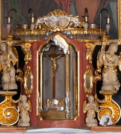 Zdjęcie nr 4: Ołtarz trójosiowy, dwukondygnacyjny z bramkami o formach architektonicznych, uszaty. Mensa murowana, prostopadłościenna z drewnianym antepedium ujętym profilowaną ramą z malowaną dekoracją roślinną. W polu malowane na płótnie przedstawienie adoracji Najświętszego Sakramentu. Tabernakulum w formie prostopadłościanu, o wypukłej ściance frontowej, ujętej pilastrami o kapitelach w formie akantowych konsol podtrzymujących pełne belkowanie. Na trzonach owalne lustra w akantowych ramach. W zwieńczeniu dwie uskrzydlone główki anielskie. Na metalowych drzwiczkach krucyfiks oraz kielich z hostią w otoczeniu winnych gron i kłosów (na odwrociu). Naroża tabernakulum flankuje para aniołów ustawionych na wolutowych konsolach. Nastawa umieszczona na wysokim cokole z bramkami mieszczącymi obrazy Chrystusa w typie Ecce Homo (z lewej) oraz Matki Boskiej Bolesnej (z prawej). Cokół artykułowany wysokimi postumentami, na których ustawione są kolumny. W polach postumentów złocona dekoracja akantowa. Kondygnacja pierwsza trójosiowa, artykułowana złoconymi kolumnami o korynckich kapitelach, ujęta srebrzonymi akantowymi uszami (suchy akant). Kolumny dźwigają pełne belkowanie, wyłamane na osiach podpór oraz odcinki przyczółka, na których siedzą figury aniołów w białych szatach. Dodatkowo, w osiach kolumn umieszczone mniejsze figury klęczących aniołów (osie wewnętrzne) oraz marmoryzowane, owalne kartusze ujęte złoconymi ramami z ornamentem małżowinowo-chrząstkowym (osie zewnętrzne). W partii fryzu złocone rozetki oraz marmoryzowane, owalne kartusze ujęte złoconym akantem. Gzyms profilowany, dekorowany dodatkowo złoconym kimationem. W polu środkowym prostokątny obraz przedstawiający Rodzinę Marii. Na zasuwie umieszczony obraz z wizerunkiem św. Katarzyny Aleksandryjskiej. Powyżej, w osi ołtarza obraz ze sceną Koronacji Marii, o nieregularnym kształcie w akantowej ramie, zwieńczonej koroną. W osiach bocznych umieszczone skrzydła boczne dawnego, gotyckiego tryptyku z wizerunkami św. Jana Chrzciciela i św. Barbary (z lewej) oraz św. Stanisława biskupa i św. Katarzyny Aleksandryjskiej (z prawej). Zwieńczenie ołtarza w formie edikuli ujętej złoconymi, korynckimi kolumnami oraz złoconymi, akantowymi uszami. Po bokach niewielkie figury klęczących aniołów. Podpory dźwigają wyłamane belkowanie dekorowane kimationem i rozetkami, łukowato wyginające się w osi ołtarza. W polu obraz w kształcie stojącego prostokąta zamkniętego łukiem półkolistym ze sceną Zwiastowania. Całość zwieńczona srebrzonym baldachimem z podwieszonej tkaniny przewiązanej złotym sznurem ze złoconą koroną umieszczoną na szczycie. Struktura ołtarza marmoryzowana w odcieniu ciemnoszarym, profile i płyciny na filarach marmoryzowane w kolorze bordowym, ornamentyka złocona i posrebrzana.