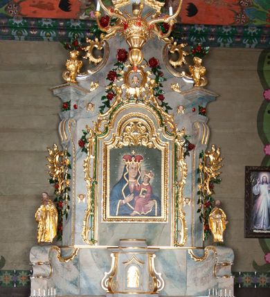 Zdjęcie nr 1: Nastawa ołtarzowa drewniana, architektoniczna, jednoosiowa, jednokondygnacyjna ze zwieńczeniem. Mensa w typie sarkofagowym, wklęsło-wypukła, zwężająca się ku dołowi, zamknięta gzymsem; naroża ujęte fragmentami rocaille'u, na froncie rocaille’owy kartusz; portatyl z marmuru dębnickiego. Na mensie ustawiono tabernakulum w formie prostopadłościennej skrzynki, o wypukłej ściance frontowej, która jest ujęta w narożach ustawionymi pod kątem pilastrami na cokołach, których trzony przyjmują formę spływów wolutowych. Podpory dźwigają gzyms, opasujący całą skrzynkę, wyłamany na ich osi. Drzwiczki w formie stojącego prostokąta zamkniętego łukiem nadwieszonym, w polu nisza z płaskorzeźbionym przedstawieniem kielicha z hostią w glorii. Drzwiczki zostały ujęte płyciną w formie stojącego prostokąta zamkniętego łukiem kotarowym dwudzielnym. Na tabernakulum tron wystawienia w postaci cokołu. Nastawa ołtarzowa została posadowiona na wysokim cokole, przyjmującym po bokach formę wolut stanowiących podstawę dla figur św. Piotra z prawej i św. Pawła z lewej strony. Jest ujęta parą pilastrów ustawionych pod katem względem lica, których trzony u góry przechodzą w woluty. Podpory dźwigają imposty. W polu środkowym płycina w formie stojącego prostokąta zamkniętego łukiem półkolistym nadwieszonym z uskokiem, w której znajduje się mniejsza nisza o tej samej formie, ujęta ramą, wypełniona obrazem Matki Boskiej z Dzieciątkiem. Zwieńczenie w formie zbliżonej do trapezu, ujętego podwójnymi spływami wolutowymi, zamkniętego falistym gzymsem. Całość wieńczy rzeźbiona gołębica Ducha Świętego w glorii promienistej. Trzony pilastrów nastawy dekorowane zwisami z różanych gałązek. Płycina pola środkowego ujęta rocaille'em, który ponad łukiem, w polu zwieńczenia, tworzy medalion z uskrzydloną główką anielską, otoczony dużymi różanymi gałązkami; w polu środkowym cztery uskrzydlone główki anielskie. Kondygnacja flankowana uszami utworzonymi z płomienistego rocaille'u i różanych gałązek. Na belkowaniu dwa rokokowe wazony z różami. Zwieńczenie ujęte falbanką, rocaille'em i różanymi gałązkami. Struktura w całości marmoryzowana w kolorze szaroniebieskim, ornamentyki i profile złocone i srebrzone, ukwiecone gałązki laserunkowe.