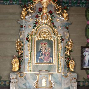 Zdjęcie nr 1: Nastawa ołtarzowa drewniana, architektoniczna, jednoosiowa, jednokondygnacyjna ze zwieńczeniem. Mensa w typie sarkofagowym, wklęsło-wypukła, zwężająca się ku dołowi, zamknięta gzymsem; naroża ujęte fragmentami rocaille&#039;u, na froncie rocaille’owy kartusz; portatyl z marmuru dębnickiego. Na mensie ustawiono tabernakulum w formie prostopadłościennej skrzynki, o wypukłej ściance frontowej, która jest ujęta w narożach ustawionymi pod kątem pilastrami na cokołach, których trzony przyjmują formę spływów wolutowych. Podpory dźwigają gzyms, opasujący całą skrzynkę, wyłamany na ich osi. Drzwiczki w formie stojącego prostokąta zamkniętego łukiem nadwieszonym, w polu nisza z płaskorzeźbionym przedstawieniem kielicha z hostią w glorii. Drzwiczki zostały ujęte płyciną w formie stojącego prostokąta zamkniętego łukiem kotarowym dwudzielnym. Na tabernakulum tron wystawienia w postaci cokołu. Nastawa ołtarzowa została posadowiona na wysokim cokole, przyjmującym po bokach formę wolut stanowiących podstawę dla figur św. Piotra z prawej i św. Pawła z lewej strony. Jest ujęta parą pilastrów ustawionych pod katem względem lica, których trzony u góry przechodzą w woluty. Podpory dźwigają imposty. W polu środkowym płycina w formie stojącego prostokąta zamkniętego łukiem półkolistym nadwieszonym z uskokiem, w której znajduje się mniejsza nisza o tej samej formie, ujęta ramą, wypełniona obrazem Matki Boskiej z Dzieciątkiem. Zwieńczenie w formie zbliżonej do trapezu, ujętego podwójnymi spływami wolutowymi, zamkniętego falistym gzymsem. Całość wieńczy rzeźbiona gołębica Ducha Świętego w glorii promienistej. Trzony pilastrów nastawy dekorowane zwisami z różanych gałązek. Płycina pola środkowego ujęta rocaille&#039;em, który ponad łukiem, w polu zwieńczenia, tworzy medalion z uskrzydloną główką anielską, otoczony dużymi różanymi gałązkami; w polu środkowym cztery uskrzydlone główki anielskie. Kondygnacja flankowana uszami utworzonymi z płomienistego rocaille&#039;u i różanych gałązek. Na belkowaniu dwa rokokowe wazony z różami. Zwieńczenie ujęte falbanką, rocaille&#039;em i różanymi gałązkami. Struktura w całości marmoryzowana w kolorze szaroniebieskim, ornamentyki i profile złocone i srebrzone, ukwiecone gałązki laserunkowe.