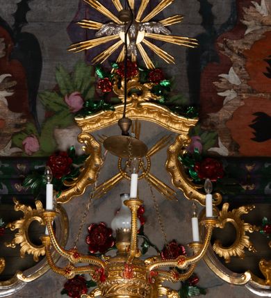 Zdjęcie nr 14: Nastawa ołtarzowa drewniana, architektoniczna, jednoosiowa, jednokondygnacyjna ze zwieńczeniem. Mensa w typie sarkofagowym, wklęsło-wypukła, zwężająca się ku dołowi, zamknięta gzymsem; naroża ujęte fragmentami rocaille'u, na froncie rocaille’owy kartusz; portatyl z marmuru dębnickiego. Na mensie ustawiono tabernakulum w formie prostopadłościennej skrzynki, o wypukłej ściance frontowej, która jest ujęta w narożach ustawionymi pod kątem pilastrami na cokołach, których trzony przyjmują formę spływów wolutowych. Podpory dźwigają gzyms, opasujący całą skrzynkę, wyłamany na ich osi. Drzwiczki w formie stojącego prostokąta zamkniętego łukiem nadwieszonym, w polu nisza z płaskorzeźbionym przedstawieniem kielicha z hostią w glorii. Drzwiczki zostały ujęte płyciną w formie stojącego prostokąta zamkniętego łukiem kotarowym dwudzielnym. Na tabernakulum tron wystawienia w postaci cokołu. Nastawa ołtarzowa została posadowiona na wysokim cokole, przyjmującym po bokach formę wolut stanowiących podstawę dla figur św. Piotra z prawej i św. Pawła z lewej strony. Jest ujęta parą pilastrów ustawionych pod katem względem lica, których trzony u góry przechodzą w woluty. Podpory dźwigają imposty. W polu środkowym płycina w formie stojącego prostokąta zamkniętego łukiem półkolistym nadwieszonym z uskokiem, w której znajduje się mniejsza nisza o tej samej formie, ujęta ramą, wypełniona obrazem Matki Boskiej z Dzieciątkiem. Zwieńczenie w formie zbliżonej do trapezu, ujętego podwójnymi spływami wolutowymi, zamkniętego falistym gzymsem. Całość wieńczy rzeźbiona gołębica Ducha Świętego w glorii promienistej. Trzony pilastrów nastawy dekorowane zwisami z różanych gałązek. Płycina pola środkowego ujęta rocaille'em, który ponad łukiem, w polu zwieńczenia, tworzy medalion z uskrzydloną główką anielską, otoczony dużymi różanymi gałązkami; w polu środkowym cztery uskrzydlone główki anielskie. Kondygnacja flankowana uszami utworzonymi z płomienistego rocaille'u i różanych gałązek. Na belkowaniu dwa rokokowe wazony z różami. Zwieńczenie ujęte falbanką, rocaille'em i różanymi gałązkami. Struktura w całości marmoryzowana w kolorze szaroniebieskim, ornamentyki i profile złocone i srebrzone, ukwiecone gałązki laserunkowe.