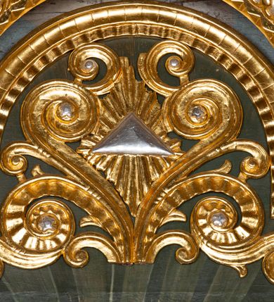 Zdjęcie nr 13: Nastawa ołtarzowa drewniana, architektoniczna, jednoosiowa, jednokondygnacyjna ze zwieńczeniem. Mensa w typie sarkofagowym, wklęsło-wypukła, zwężająca się ku dołowi, zamknięta gzymsem; naroża ujęte fragmentami rocaille&#039;u, na froncie rocaille’owy kartusz; portatyl z marmuru dębnickiego. Na mensie ustawiono tabernakulum w formie prostopadłościennej skrzynki, o wypukłej ściance frontowej, która jest ujęta w narożach ustawionymi pod kątem pilastrami na cokołach, których trzony przyjmują formę spływów wolutowych. Podpory dźwigają gzyms, opasujący całą skrzynkę, wyłamany na ich osi. Drzwiczki w formie stojącego prostokąta zamkniętego łukiem nadwieszonym, w polu nisza z płaskorzeźbionym przedstawieniem kielicha z hostią w glorii. Drzwiczki zostały ujęte płyciną w formie stojącego prostokąta zamkniętego łukiem kotarowym dwudzielnym. Na tabernakulum tron wystawienia w postaci cokołu. Nastawa ołtarzowa została posadowiona na wysokim cokole, przyjmującym po bokach formę wolut stanowiących podstawę dla figur św. Piotra z prawej i św. Pawła z lewej strony. Jest ujęta parą pilastrów ustawionych pod katem względem lica, których trzony u góry przechodzą w woluty. Podpory dźwigają imposty. W polu środkowym płycina w formie stojącego prostokąta zamkniętego łukiem półkolistym nadwieszonym z uskokiem, w której znajduje się mniejsza nisza o tej samej formie, ujęta ramą, wypełniona obrazem Matki Boskiej z Dzieciątkiem. Zwieńczenie w formie zbliżonej do trapezu, ujętego podwójnymi spływami wolutowymi, zamkniętego falistym gzymsem. Całość wieńczy rzeźbiona gołębica Ducha Świętego w glorii promienistej. Trzony pilastrów nastawy dekorowane zwisami z różanych gałązek. Płycina pola środkowego ujęta rocaille&#039;em, który ponad łukiem, w polu zwieńczenia, tworzy medalion z uskrzydloną główką anielską, otoczony dużymi różanymi gałązkami; w polu środkowym cztery uskrzydlone główki anielskie. Kondygnacja flankowana uszami utworzonymi z płomienistego rocaille&#039;u i różanych gałązek. Na belkowaniu dwa rokokowe wazony z różami. Zwieńczenie ujęte falbanką, rocaille&#039;em i różanymi gałązkami. Struktura w całości marmoryzowana w kolorze szaroniebieskim, ornamentyki i profile złocone i srebrzone, ukwiecone gałązki laserunkowe.